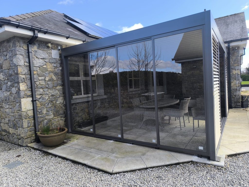 Aluminium pergola with sliding glass walls beside a stone cottage in Ireland